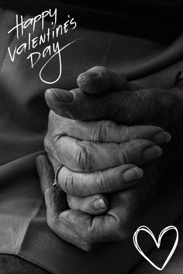 Elderly couple holding hands with ‘Happy Valentine’s Day’ written in cursive, symbolizing love, caregiving, and devotion on Valentine’s Day.