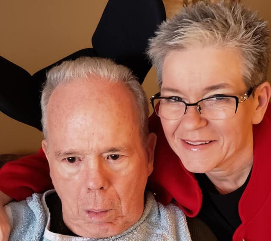 Lura Sawyer smiling beside her husband Pete, who is living with ALS, sharing a moment together in their home