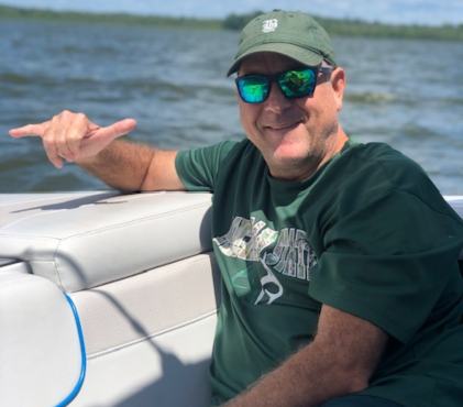 Mike Foster on a boat in California, smiling and pointing in Michigan State gear