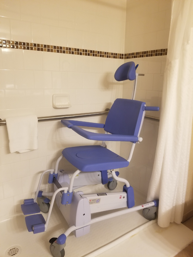 ADA-compliant roll-in shower with a secure blue shower chair and grab bars, designed for safe bathing with mobility limitations